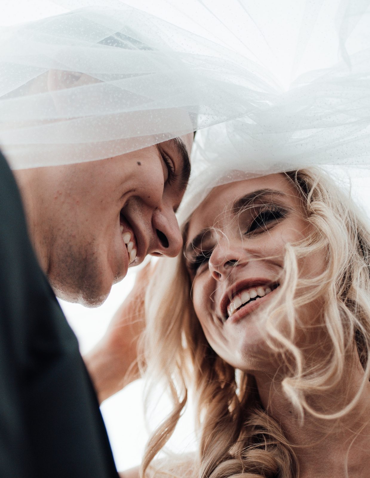 Newlyweds smiling beneath a bridal veil